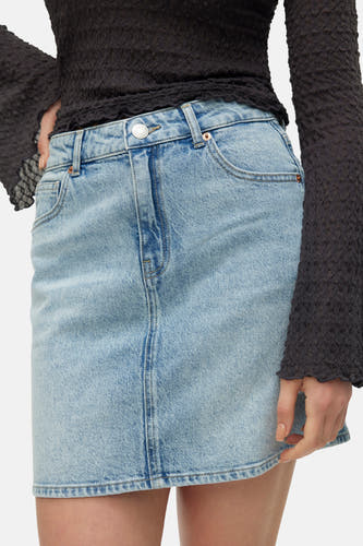 Jupe courte en denim bleu clair de VERO MODA avec bouton argenté, poches avant et portée avec un haut texturé foncé.