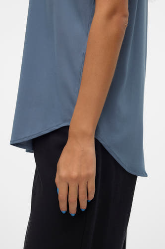 Blauw mouwloze blouse van VERO MODA®, met gladde textuur en gedragen met zwarte broek.
