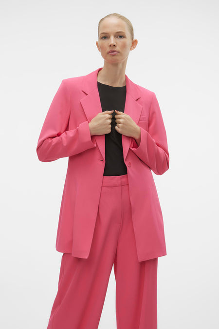 Blazer rose de VERO MODA® avec des manches longues et une fermeture à boutons, porté sur un t-shirt noir et un pantalon rose.