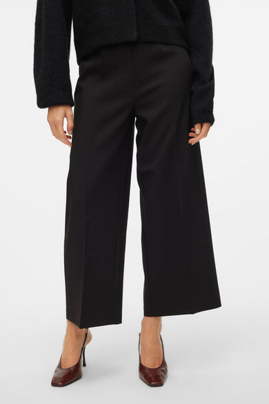 Pantalon noir de VERO MODA, associé à un cardigan noir avec un détail en tricot et des chaussures marron.