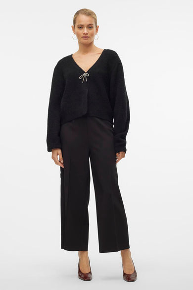 Zwarte broek van VERO MODA, gecombineerd met een zwarte cardigan met een strikdetail en bruine schoenen.
