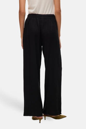 Zwarte broek van VERO MODA®, met wijde pijpen en elastische tailleband, gezien van achteren met hakken.
