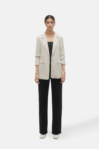 Ecru blazer van VERO MODA®, met lange mouwen, gedragen over een zwarte top en zwarte broek.