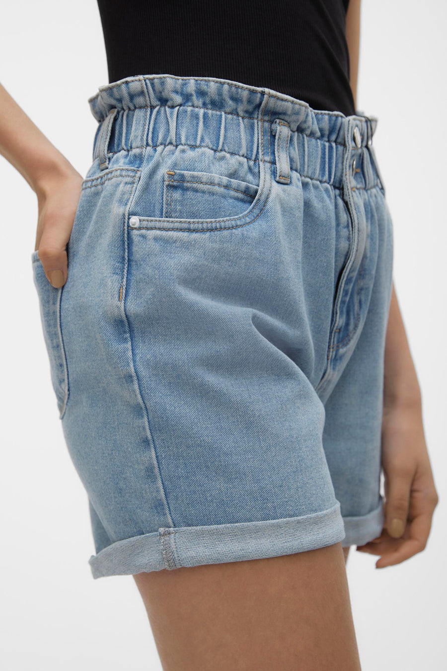 Short en jean bleu clair de VERO MODA® avec une taille élastique froncée, des poches avant et des jambes retroussées, porté avec un haut noir.