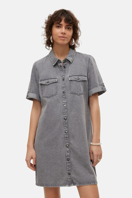 Femme en jupe denim gris avec des boutons et des bottes brunes.