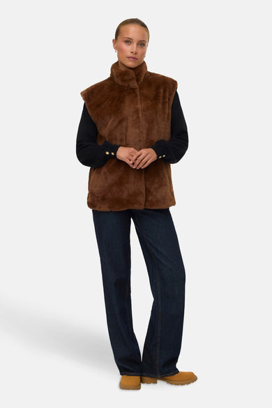 Gilet marron de VERO MODA, porté sur une chemise noire avec des boutons dorés et un jean bleu marine.