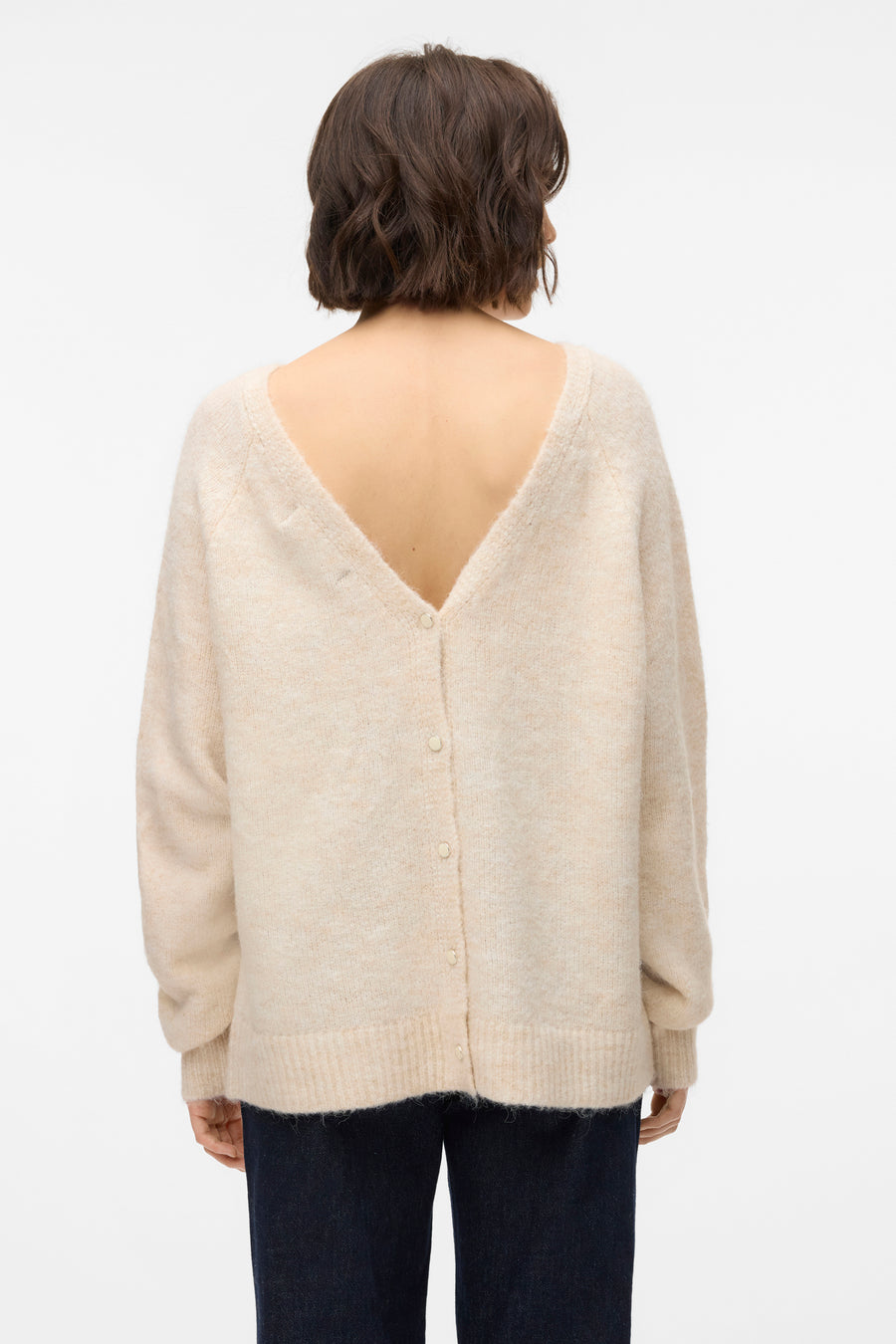 Pull beige à col rond de VERO MODA, avec longues manches et détail de bouton sur le dos, associé à un pantalon foncé.