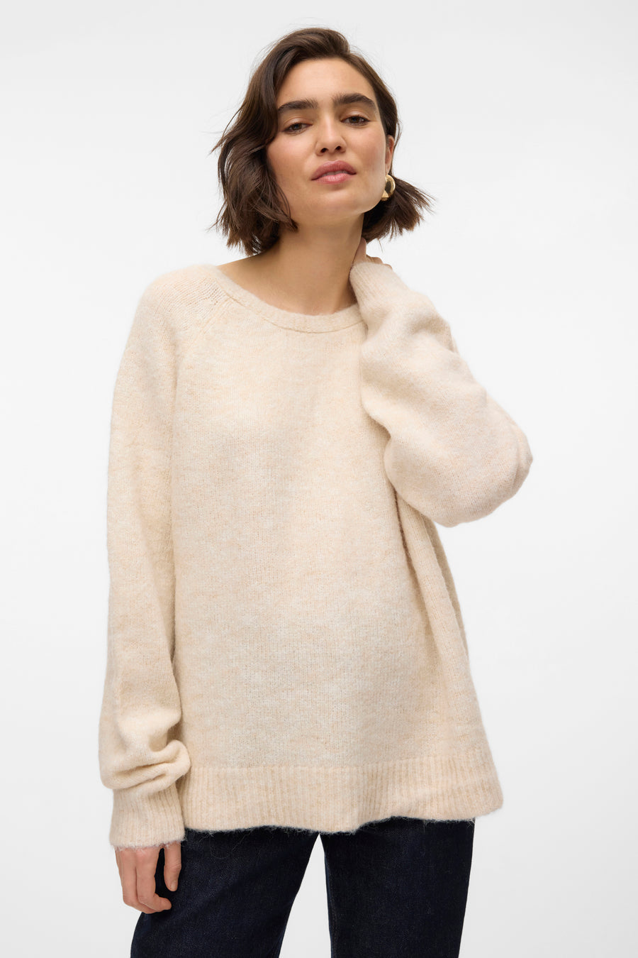 Pull beige à col rond de VERO MODA, avec des manches longues et porté avec un pantalon foncé.