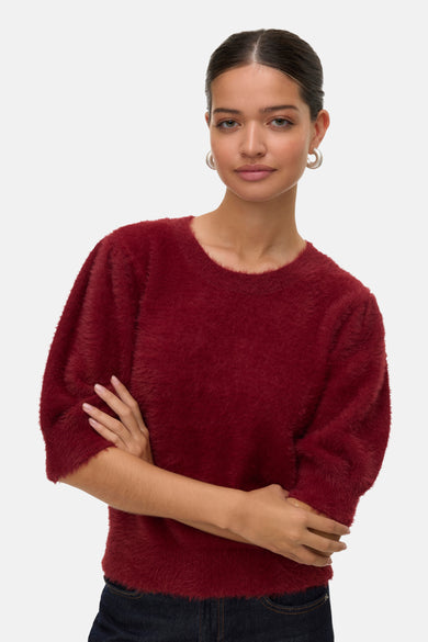T-shirt rouge à col rond de VERO MODA, texture douce, femme portant des boucles d'oreilles argentées et les bras croisés.