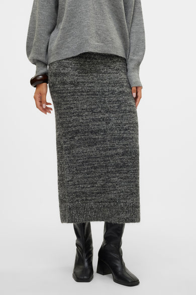 Longue jupe noire de Vero Moda, avec une texture mélangée et une fente à l'arrière, associée à des bottes et un pull gris.