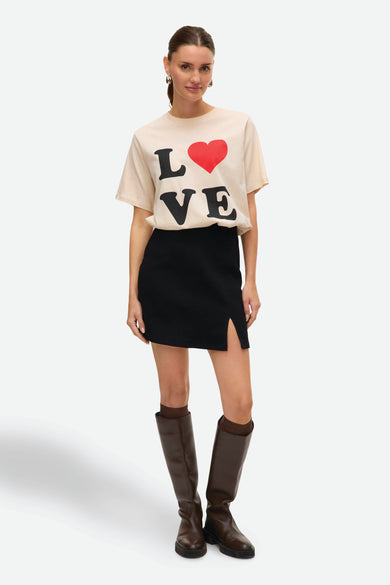 Jupe courte noire de VERO MODA, avec une fente à l'avant et associée à des bottes brunes jusqu'aux genoux.