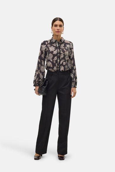 Pantalon noir de VERO MODA, avec des jambes larges et une texture lisse, associé à une blouse imprimée et une pochette.