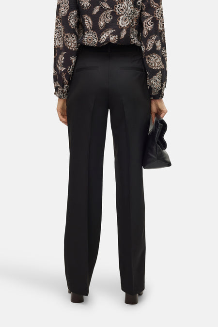 Pantalon noir de VERO MODA, vu de l'rièrerière avec une blouse à fleurs et un sac noir.