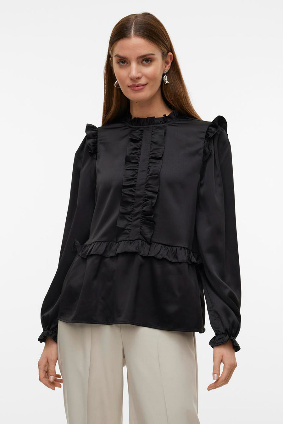Blouse noire à longues manches de Vero Moda, avec des plis sur le devant et les épaules, associée à un pantalon crème et des talons noirs.