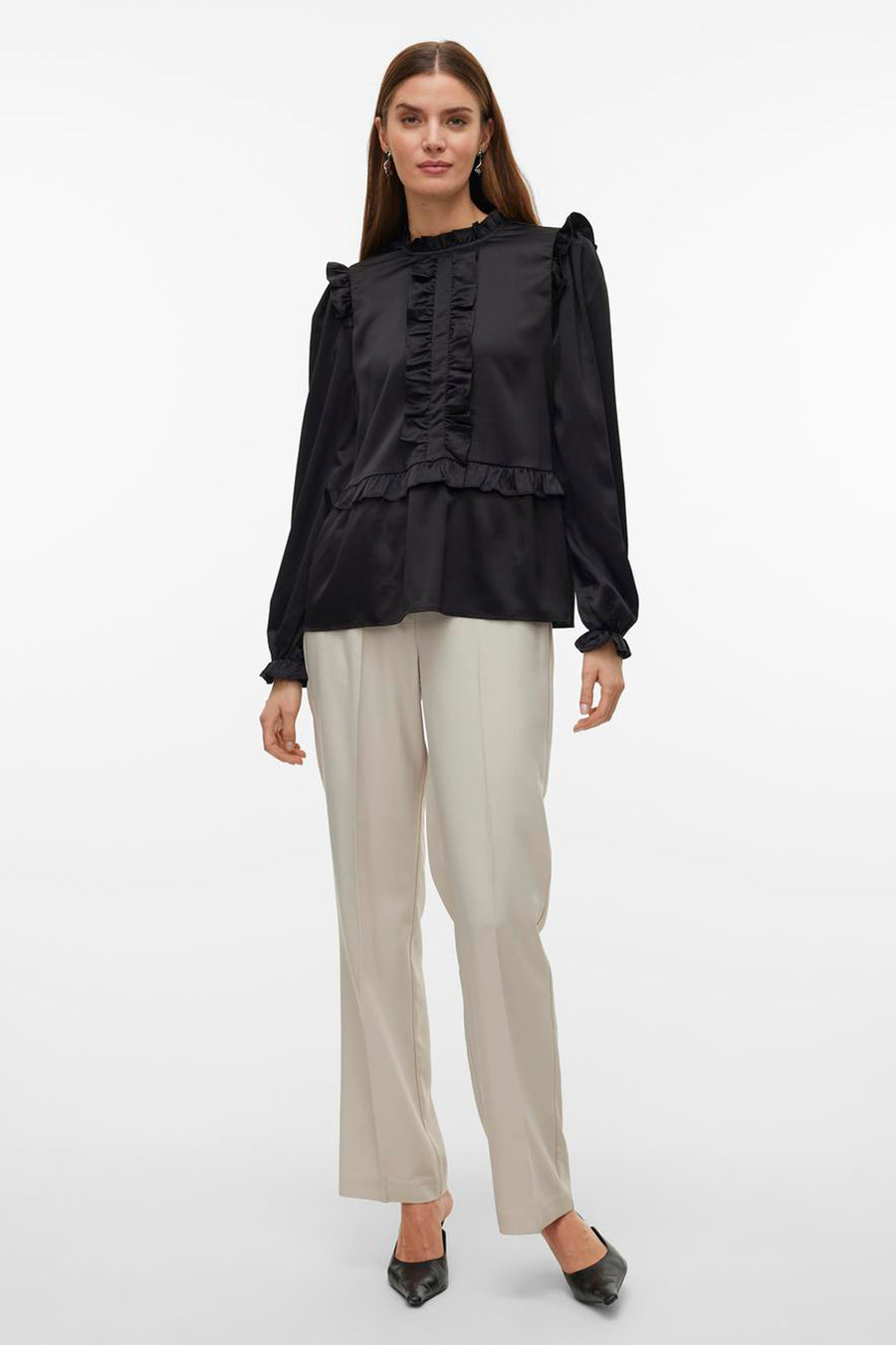 Zwarte blouse met lange mouwen van Vero Moda, met ruches langs de voorkant en schouders, gecombineerd met crèmekleurige broek en zwarte hakken.
