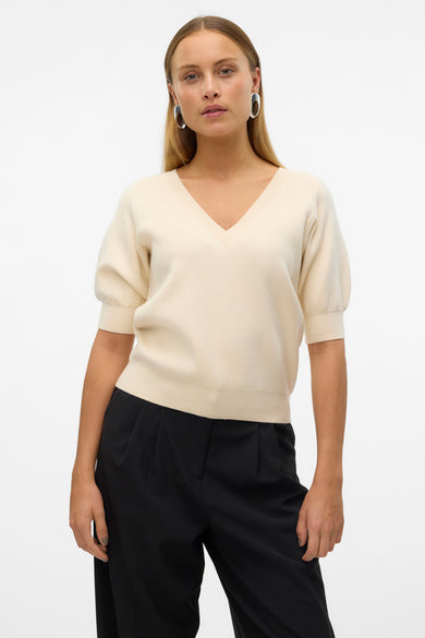 T-shirt écru avec col V de Vero Moda, associé à un pantalon noir et des boucles d'oreilles argentées.