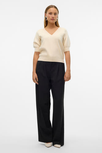 Pull écru à col V de VERO MODA®, associé à un pantalon noir et des chaussures crème.