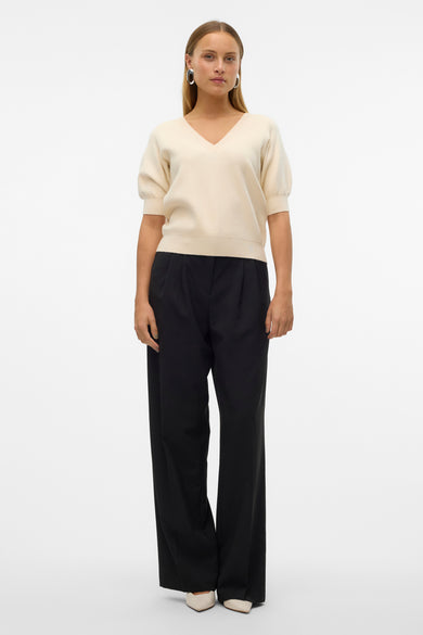 Pull écru à col V de VERO MODA®, associé à un pantalon noir et des chaussures crème.