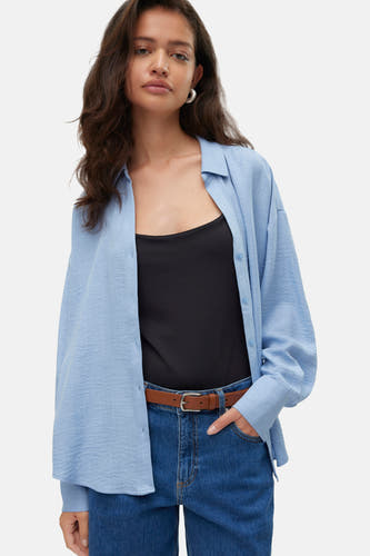 Chemise bleue à manches longues de VERO MODA portée sur une chemisier noir et des jeans.
