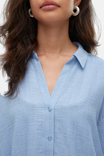 Chemise bleue à manches longues de VERO MODA, avec un col V et des boucles d'oreilles couleur argent.
