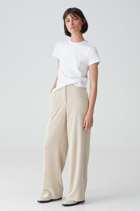 Pantalon beige OPUS à jambes larges et texture finement côtelée, porté avec un t-shirt blanc et des mocassins clairs.