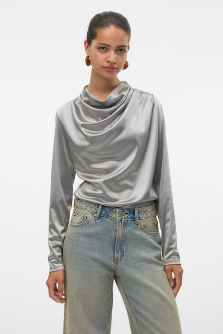 Blouse grise à longues manches de VERO MODA®, avec une ligne de col pliée, associée à des jeans larges.