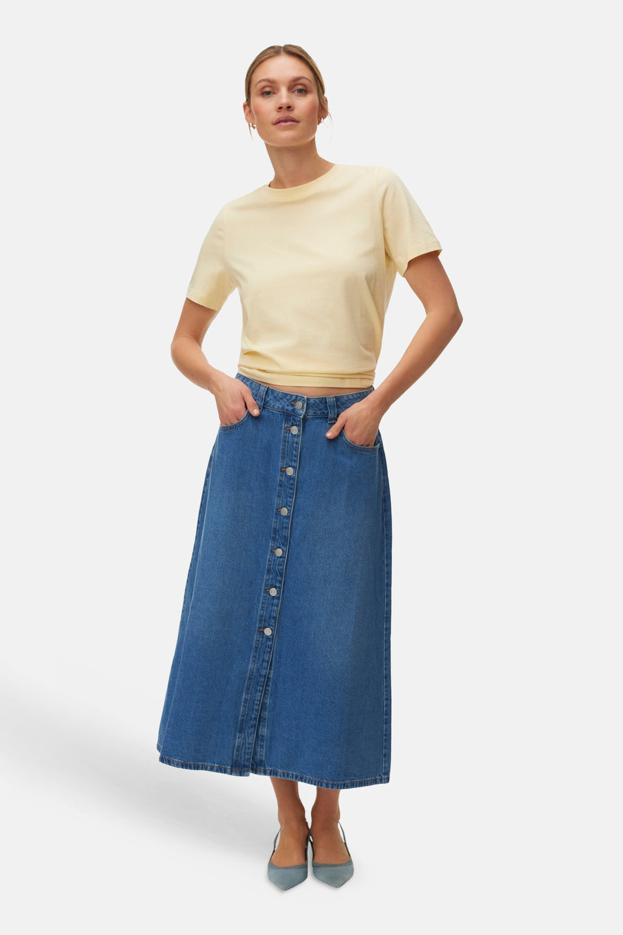 Geel T-shirt met korte mouwen van VERO MODA®, gedragen met een blauwe denim rok met knopen en bijpassende schoenen.
