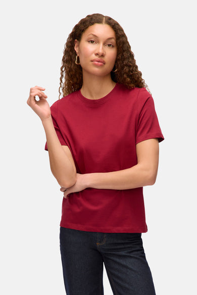 T-shirt rouge à manches courtes de VERO MODA, porté avec des jeans foncés et des boucles d'oreilles dorées.