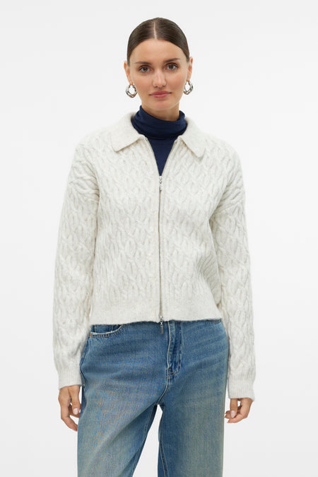 Gilet écru de Vero Moda, avec un motif côtelé, porté sur une chemise bleue et un pantalon en denim.