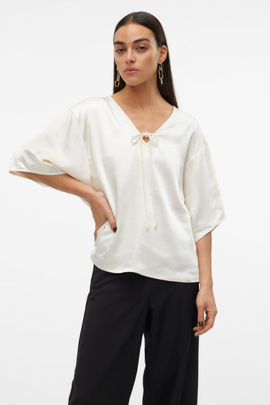 Blouse écru à manches trois-quarts de VERO MODA, avec un détail de boutons et portée avec des pantalons noirs larges et des bottines.