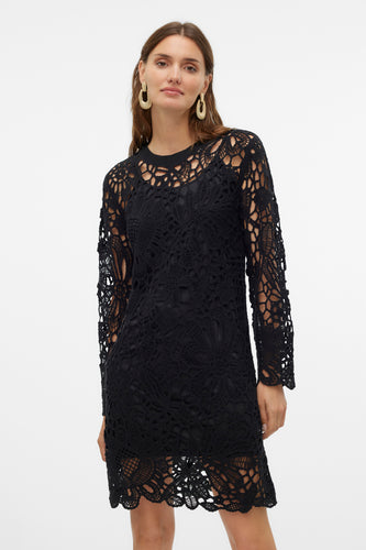 Zwarte, gehaakte jurk met lange mouwen en gouden oorbellen.