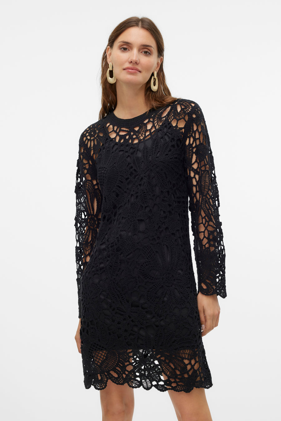 Zwarte, gehaakte jurk met lange mouwen en gouden oorbellen.