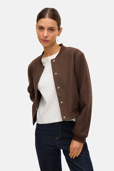 Manteau court brun de VERO MODA®, avec des boutons pression, porté avec un chemisier blanc et des jeans bleu marine.