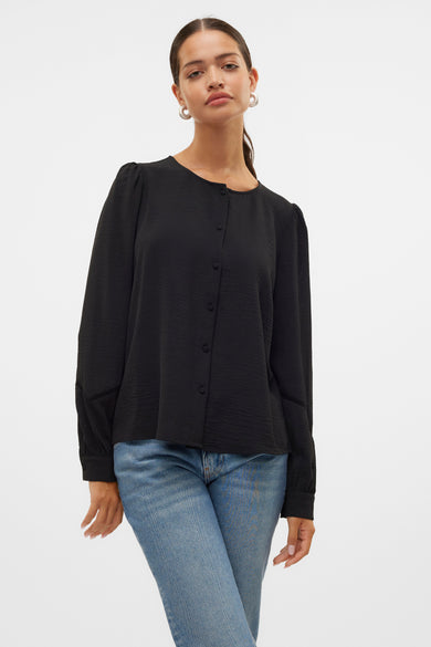Blouse noire à manches longues de VERO MODA, avec fermeture à boutons, portée avec des jeans bleus et des chaussures crème.