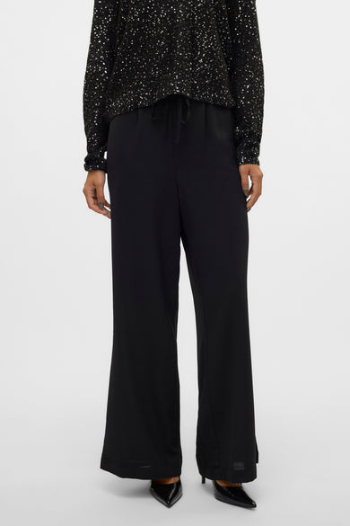 Pantalon noir de VERO MODA, associé à une chemise scintillante, avec des jambes larges et une ceinture élastiquée.
