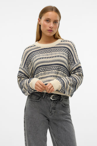 Jonge vrouw in gestreepte trui en grijze jeans met riem.