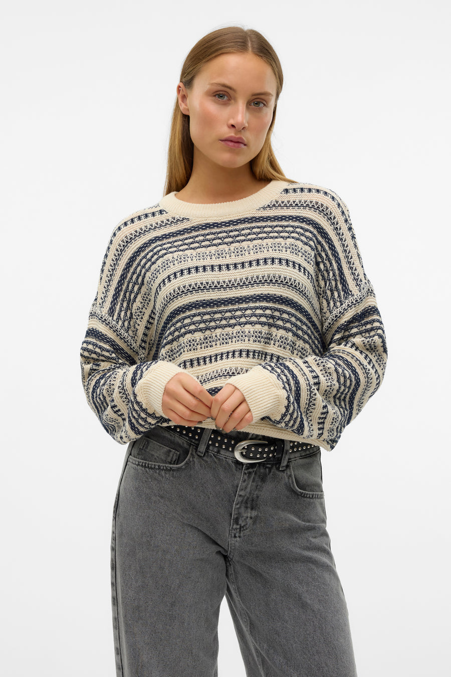 Jonge vrouw in gestreepte trui en grijze jeans met riem.