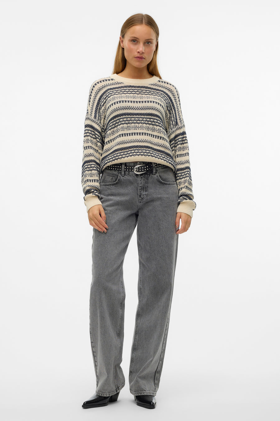 Vrouw draagt gebreide trui met grijze jeans en zwarte laarzen.