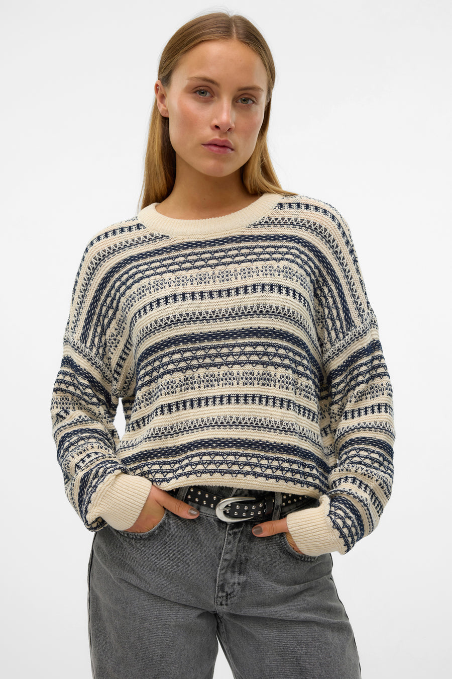 Vrouw met gestreepte trui en grijze jeans met riem.