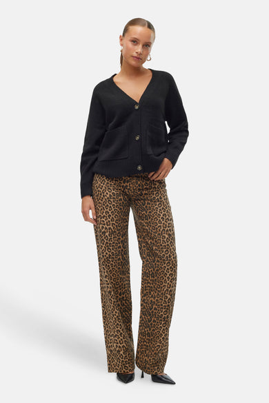 Cardigan noir de VERO MODA, avec des manches longues, une fermeture à boutons et des poches brodées, porté avec un pantalon imprimé léopard.