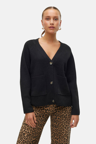 Cardigan noir de Vero Moda, avec des manches longues, une fermeture à boutons et des poches broiquées, associé à un pantalon imprimé léopard.