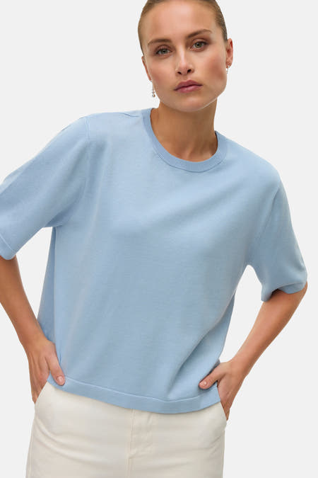 T-shirt bleu avec col rond de VERO MODA, design simple, porté avec un short blanc et des boucles d'oreilles argentées.