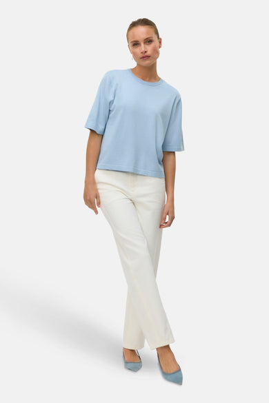 T-shirt bleu avec col rond de VERO MODA, porté avec un pantalon blanc et des chaussures bleues.