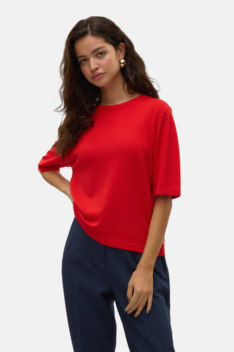 Pull rouge à col rond de VERO MODA®, porté avec un pantalon bleu foncé et des chaussures marron.