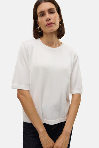 Pull blanc à col rond de VERO MODA, à manches courtes, porté avec un jean foncé et des boucles d'oreilles dorées.