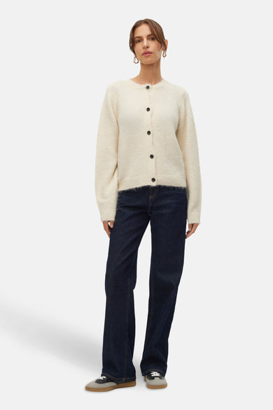 Gilet écru de VERO MODA®, avec des manches longues, une fermeture à boutons et porté avec des jeans foncés et des baskets.