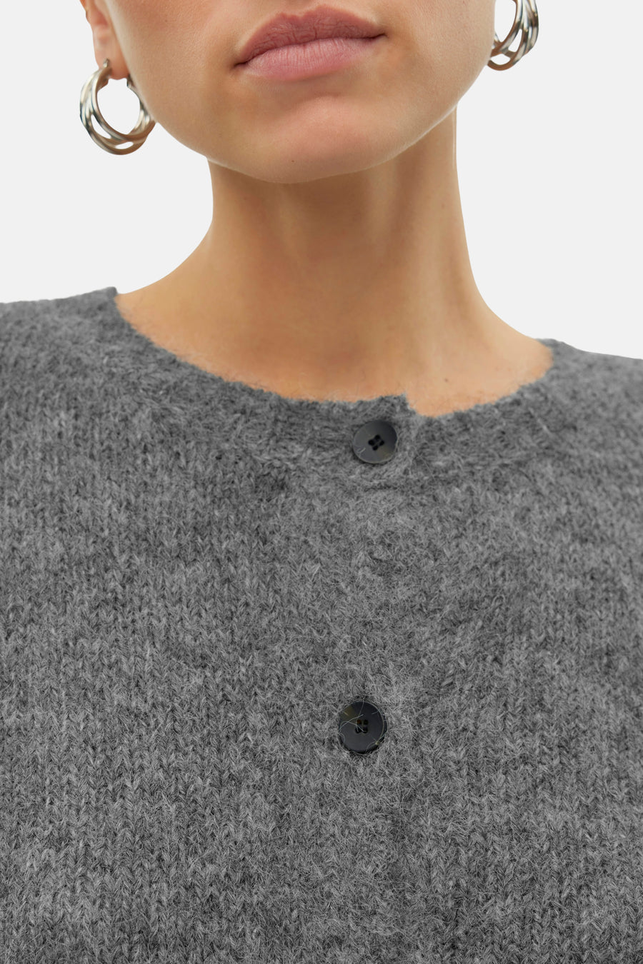 Cardigan gris de VERO MODA, avec fermeture à boutons et une texture tricotée, porté avec des boucles d'oreilles argentées.
