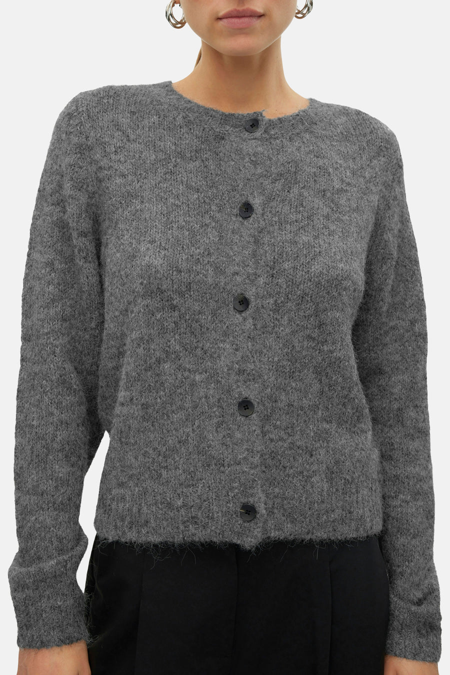 Cardigan gris de VERO MODA®, avec des manches longues et une fermeture à boutons noirs, porté sur un pantalon noir.