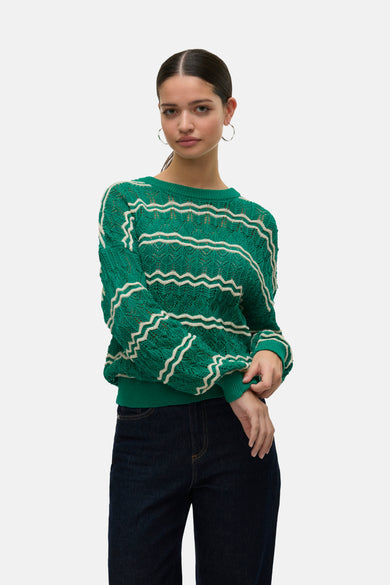 T-shirt vert avec col rond de VERO MODA, fini avec des rayures zigzag blanches et des manches longues, associé à des jeans foncés et des boucles d'oreilles argentées.