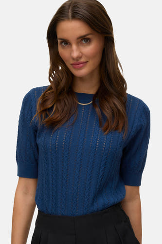 Pull bleu à col rond de Vero Moda, avec motif ajouré et manches courtes, combiné avec un pantalon noir.